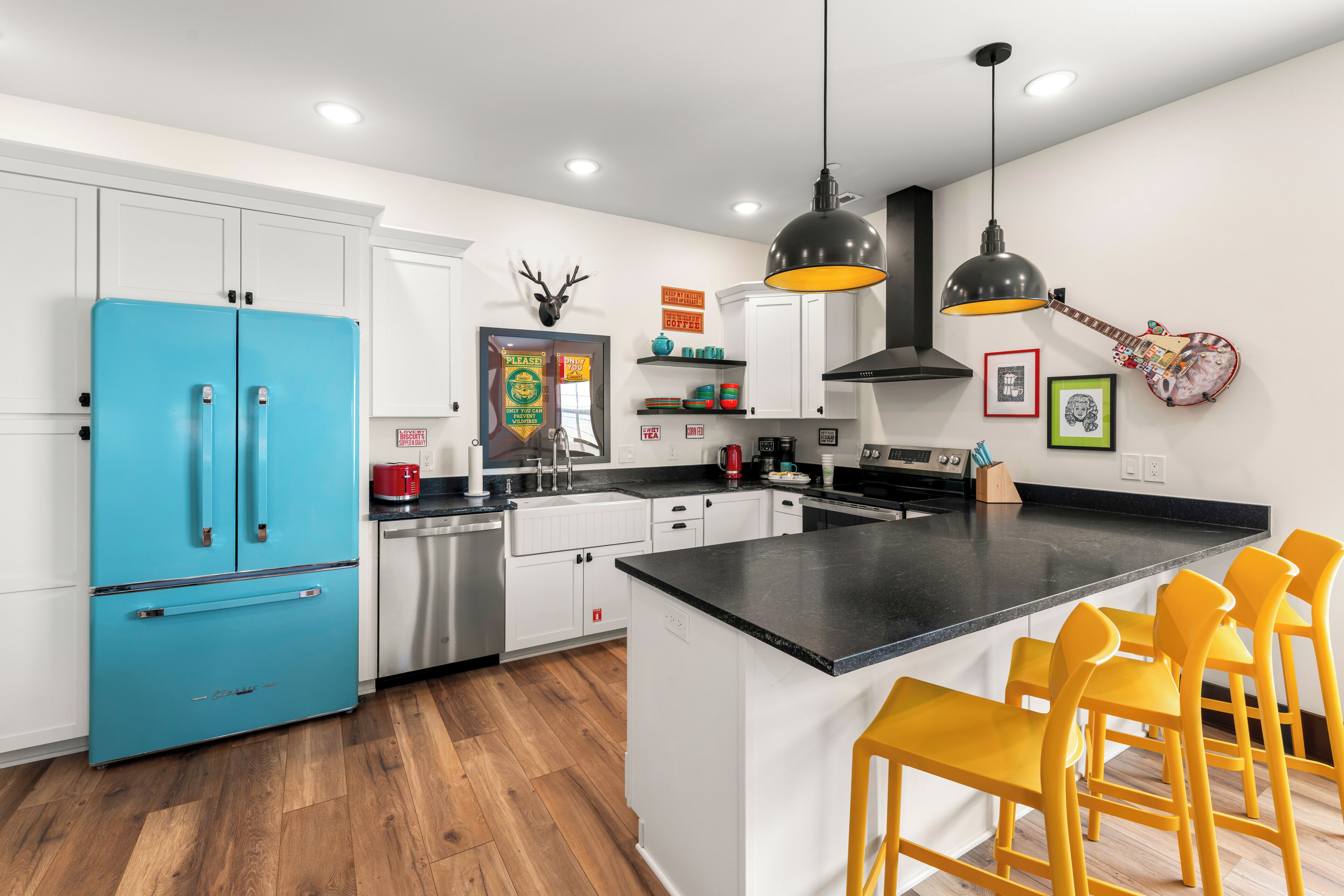 A modern kitchen with a blue refrigerator, white cabinets, a black countertop, and a central island with yellow chairs.