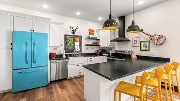 A modern kitchen with a blue refrigerator, white cabinets, a black countertop, and a central island with yellow chairs.