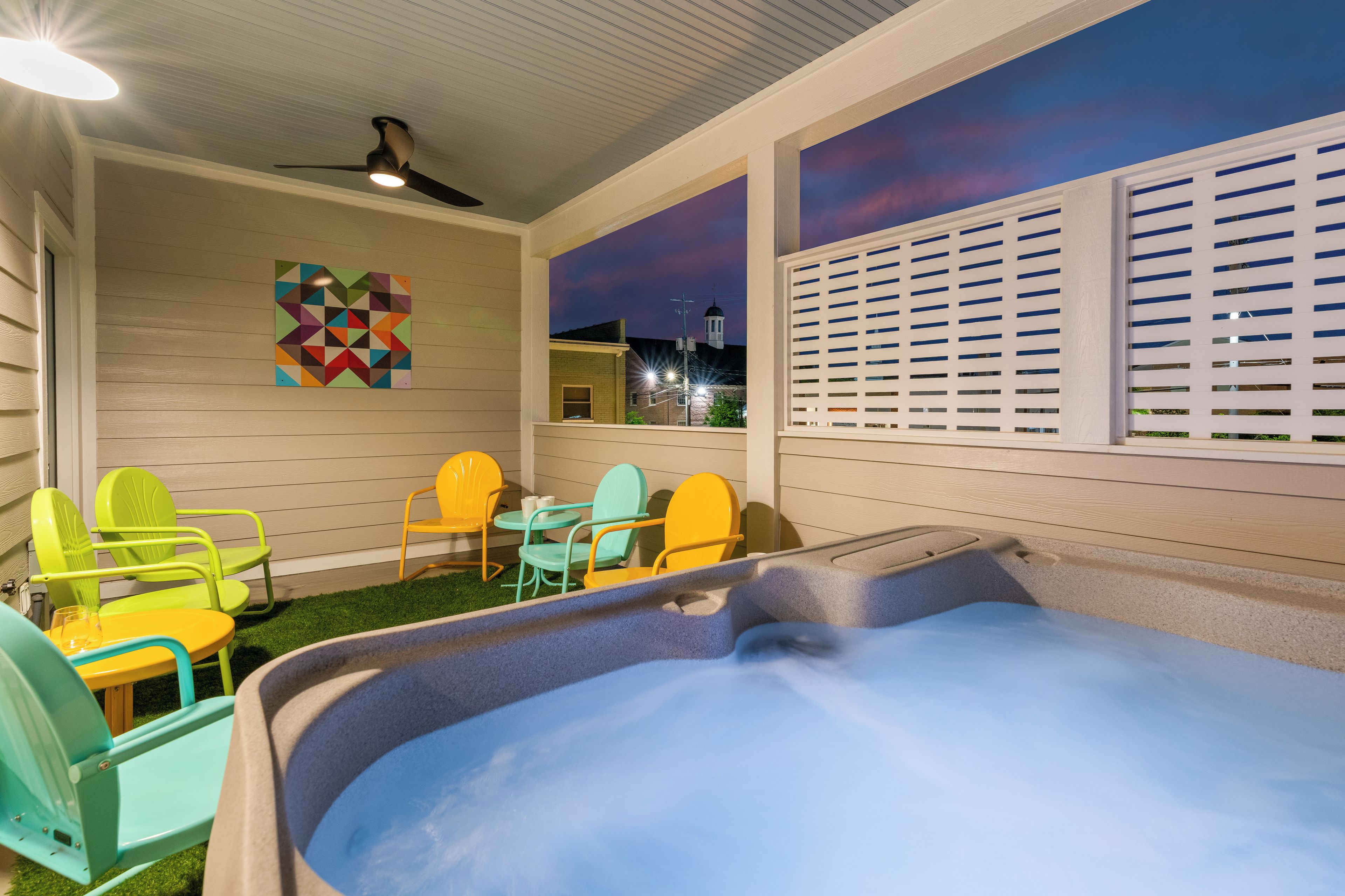 A cozy outdoor seating area with a hot tub, colorful chairs, and a ceiling fan.