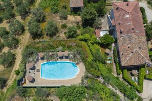 Eine Vogelperspektive zeigt ein Anwesen mit Swimmingpool, umgeben von viel Grün und einem Haus mit Ziegeldach.