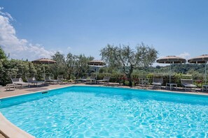 Ein Schwimmbecken mit Liegestühlen und Sonnenschirmen, umgeben von Bäumen und Hügeln.