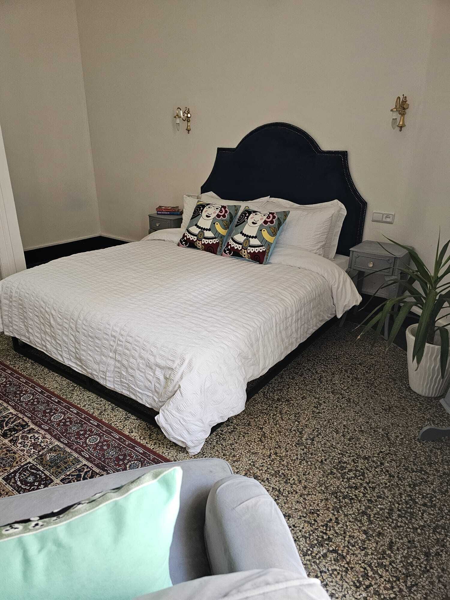 A neatly made bed with white bedding, a dark headboard, and two decorative pillows.