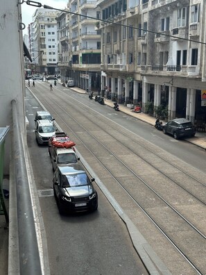Une rue avec des voies de tramway, des voitures garées et un immeuble doté de balcons.