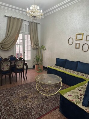 Ein Wohnzimmer mit einem runden Glastisch, einer Couch, einem Esstisch mit Stühlen und einer Chandelier.