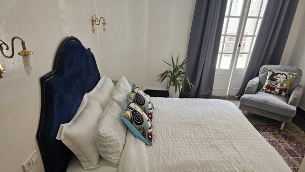 A hotel room with a bed, a chair, a nightstand, a potted plant, and a window with curtains. - Spacious 2-Bedroom Apartment in Central Casablanca – Sleeps 5 (Casablanca)