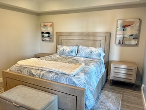 A bedroom with a bed, nightstands, a bench, and abstract wall art.