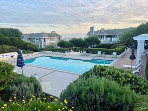Une piscine rectangulaire entourée de chaises longues et de parasols, offrant une vue sur des immeubles résidentiels et un ciel dégagé.