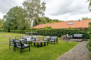 Eine Terrasse mit Gartenmöbeln, ein gepflasterter Weg und ein Haus mit Ziegeldach.
