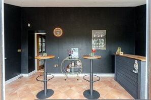 Eine Bar mit zwei Barhocker, einem kleinen runden Tisch, einem neonbeleuchteten Schild an der Wand und einem Poster.