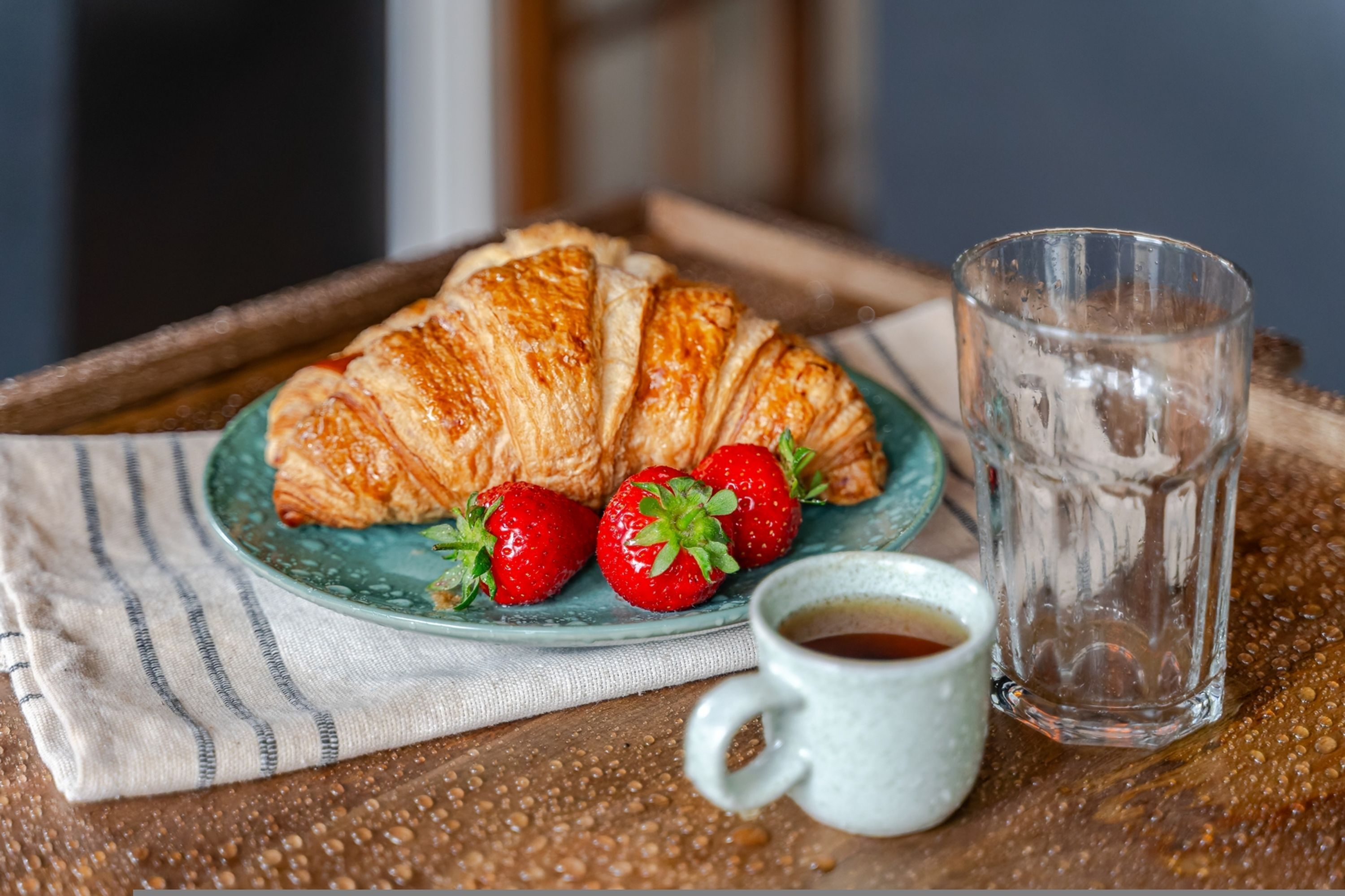 A tray with a croissant, strawberries, and a cup of coffee.