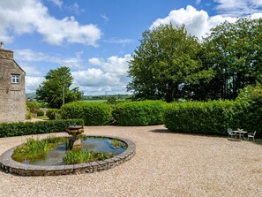 Un jardin avec un bassin circulaire, un bâtiment en pierre et une vue sur la campagne.
