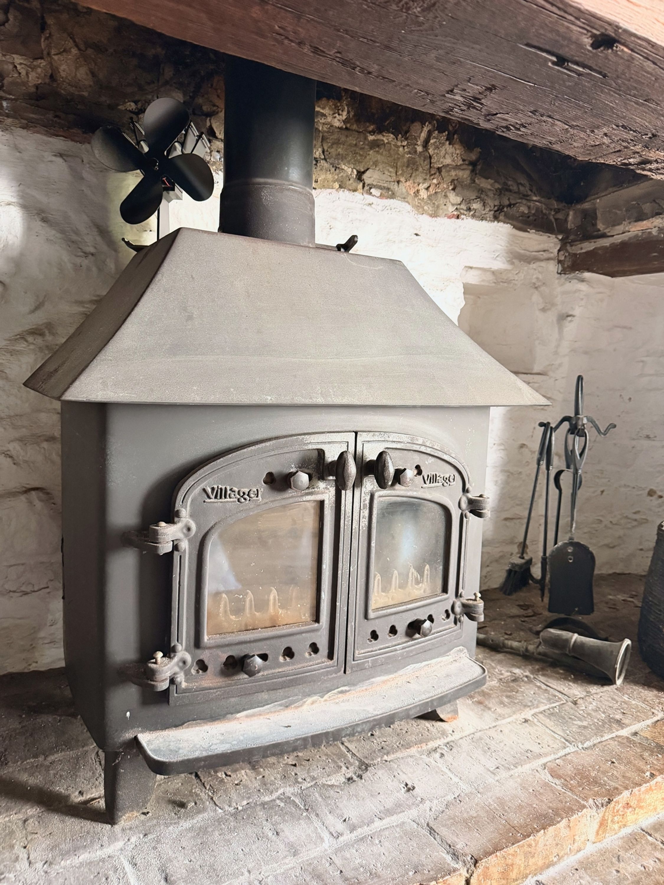 Un poêle à bois de style ancien, doté d’une cheminée, installé dans une pièce rustique aux murs de pierre et au plafond en bois.