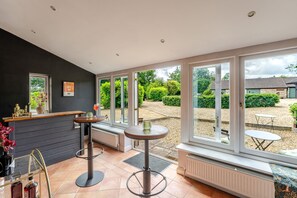 A room with a bar area, large windows, and a view of the garden. - 1641 Historic Farmhouse Sleeps 16 Bath Bristol (Bristol)