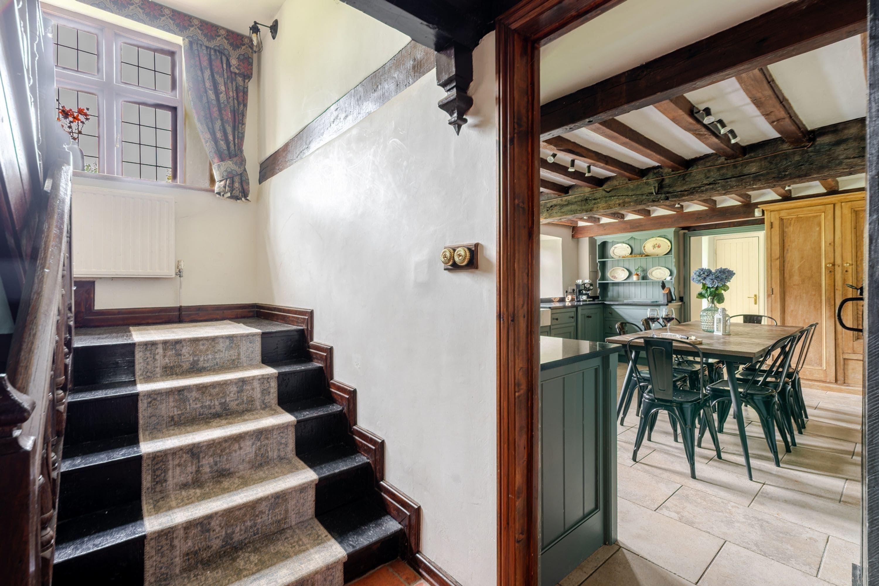 Un escalier en bois mène à une cuisine équipée d’une table et de chaises.