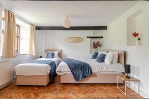 Ein Schlafzimmer mit zwei Betten, einem Nachttisch, einer Lampe und einem Fenster mit Vorhängen.