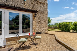 A stone building with a patio area featuring a table and chairs, a small fountain, and a view of the surrounding landscape. - 1641 Historic Farmhouse Sleeps 16 Bath Bristol (Bristol)