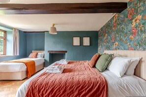 Une chambre avec deux lits, un plafond en bois, un papier peint à motifs floraux et une fenêtre avec des rideaux.