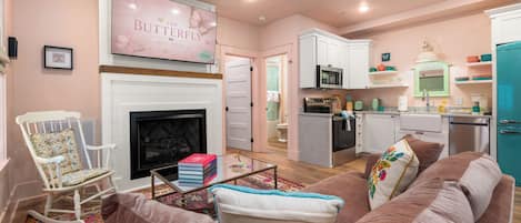 A cozy living room with a fireplace, a sofa, a rocking chair, and a kitchen area with a microwave and refrigerator.
