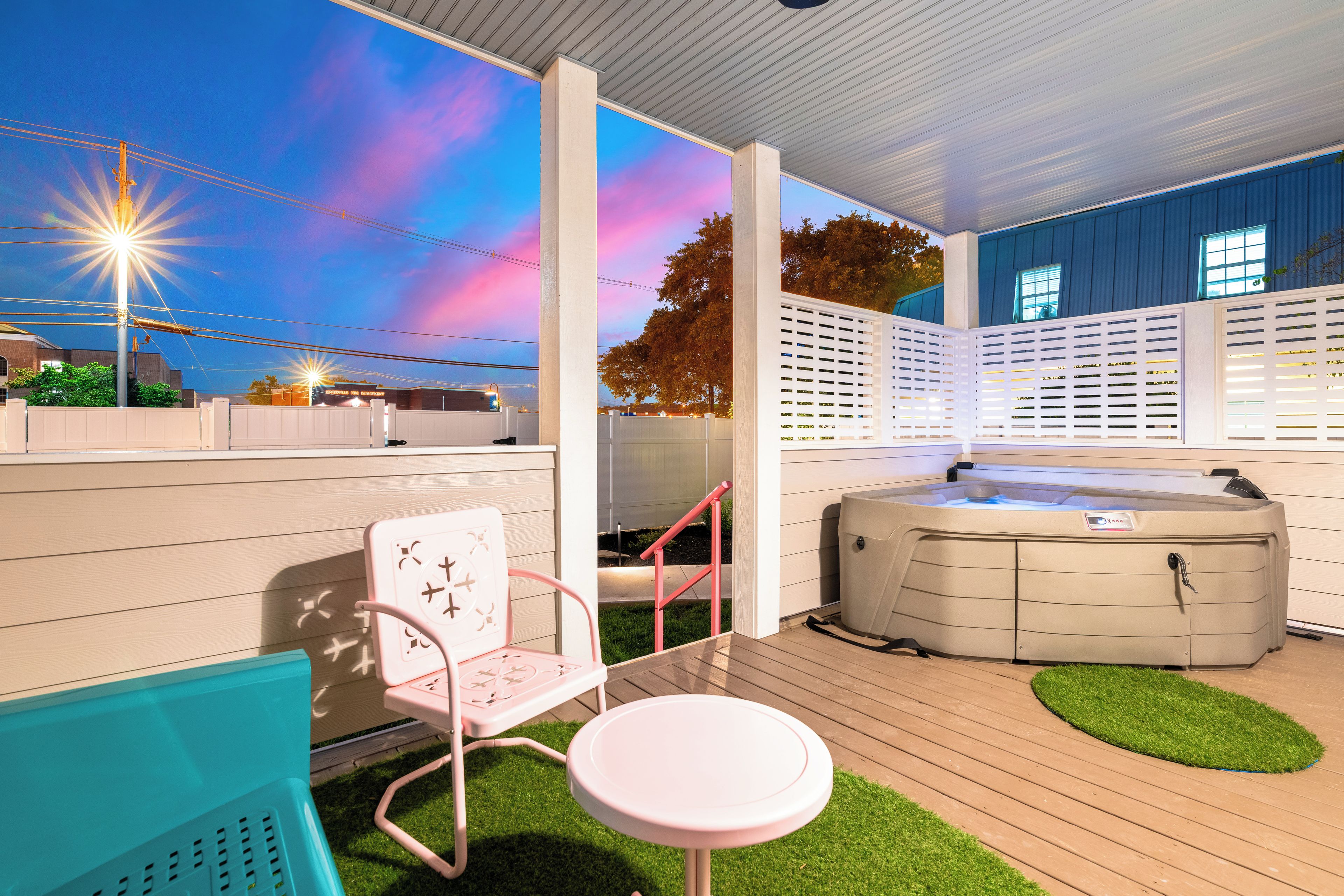 Ein Außenbereich mit Terrasse, Whirlpool, einem rosa Stuhl und einem kleinen Tisch.