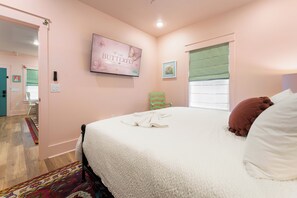 A bedroom with a bed, a television, a window with blinds, a chair, and a door leading to another room. - 1BR Hot Tub Suite • Butterfly (Sevierville)