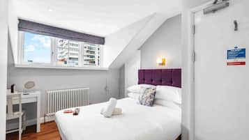 Un dormitorio con cama, ventana, radiador, mesita de noche y puerta.