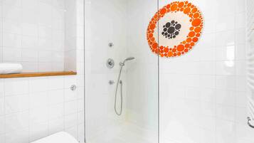 Una ducha con paredes de vidrio, pared de azulejos blancos, estante de madera y adorno circular de azulejos.