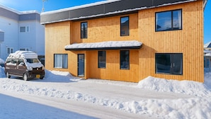 Un edificio de madera de dos pisos con un techo cubierto de nieve y un coche estacionado al frente.