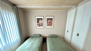 Una habitación con dos camas individuales, una ventana con persianas y dos cuadros en la pared.