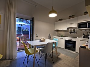 A modern kitchen with white cabinets, a microwave, and a sink. There is a dining area with a white table and chairs. - Le Terrazze sul Cortile - Red (Salerno)