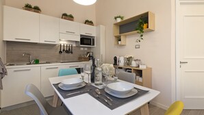 Una cucina moderna con mobili bianchi, un tavolo da pranzo apparecchiato con piatti e posate, e una lampada a sospensione gialla.