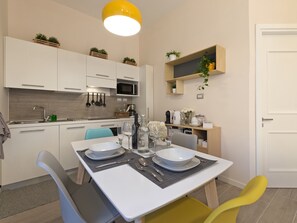 A modern kitchen with white cabinets, a dining table set with plates and cutlery, and a yellow pendant light. - Le Terrazze sul Cortile - Red (Salerno)