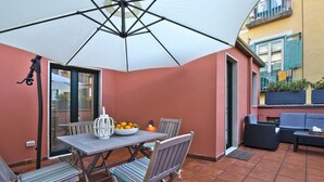 Una terrazza esterna con tavolo, sedie, una ciotola di frutta e un ombrellone bianco.