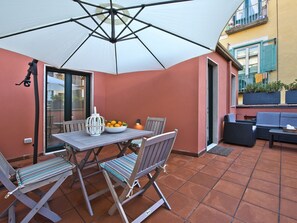 An outdoor patio with a table, chairs, a bowl of fruit, and a white umbrella. - Le Terrazze sul Cortile - Red (Salerno)