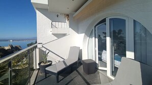 Ein Balkon mit Meerblick, eine Sitzecke mit Bank und kleinem Tisch sowie eine Glastür zu einem Innenbereich.
