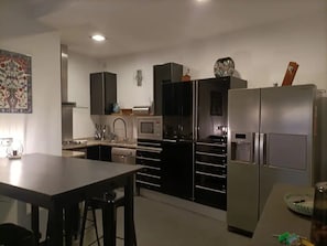 A modern kitchen with stainless steel appliances, a dining area with a table and chairs, and a decorative wall piece. - Joan Margarit 24 With 4 Bedrooms and 3 Bathrooms (Roses)