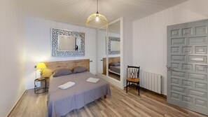 A bedroom with a bed, a chair, a lamp, a mirror, and a door. - Joan Margarit 24 With 4 Bedrooms and 3 Bathrooms (Roses)