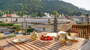 Ein Holztisch mit Teekanne, Tassen und einer Schale Erdbeeren auf einem Balkon mit Blick auf eine Hügellandschaft.