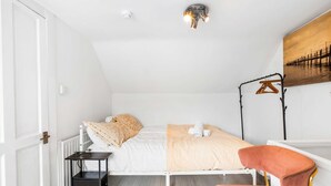 A bedroom with a bed, bedside table, chair, radiator, and a wall-mounted light fixture. - Simply Boho By My Getaways (Brighton)