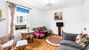 A living room with a sofa, a small table, a TV, and a window with curtains. - Simply Boho By My Getaways (Brighton)