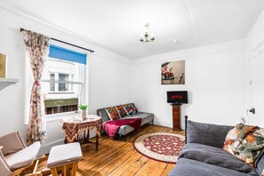 Ein Wohnzimmer mit einer Couch, einem kleinen Tisch, einem Fernseher und einem Fenster mit Vorhängen.
