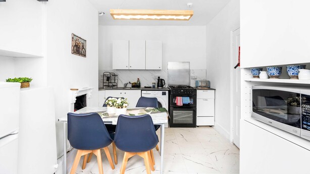 A compact kitchen with white cabinets, a dining table with chairs, a microwave, and a stove. - Simply Boho By My Getaways (Brighton)
