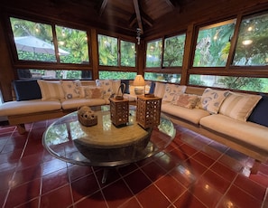 A room with a round glass coffee table, two wooden lanterns, a sofa with patterned cushions, and large windows with a view of greenery. - Cozy 4-Bedroom Villa in Casa de Campo (La Romana)
