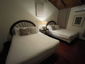 A room with two beds, each with a headboard and pillows. There is a nightstand with a lamp between the beds. - Cozy 4-Bedroom Villa in Casa de Campo (La Romana)