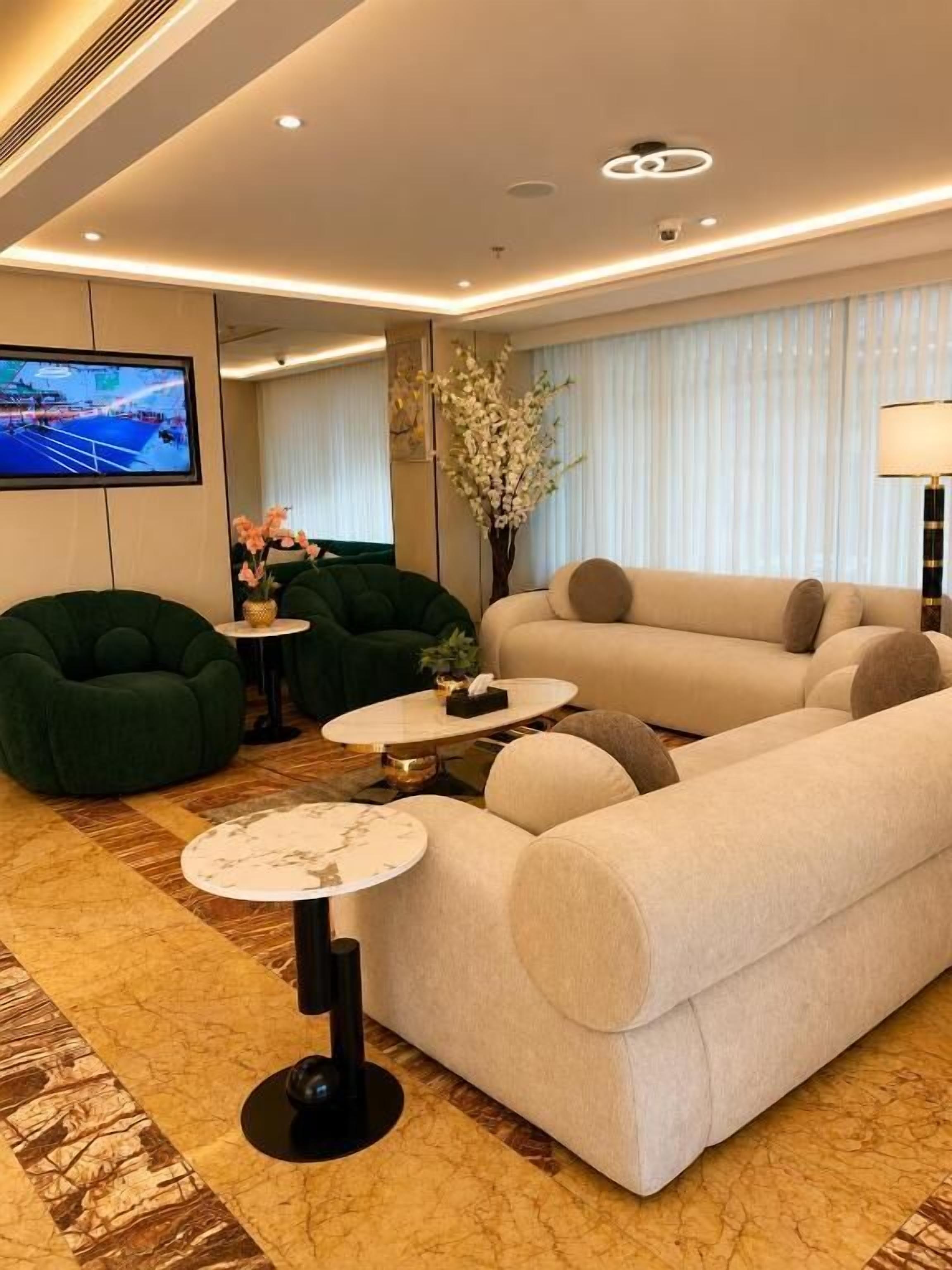 Una sala moderna con un sofá, sillones verdes, una mesa de centro y un televisor.
