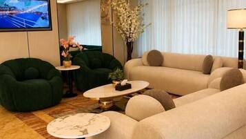 Una sala moderna con un sofá, sillones verdes, una mesa de centro y un televisor.
