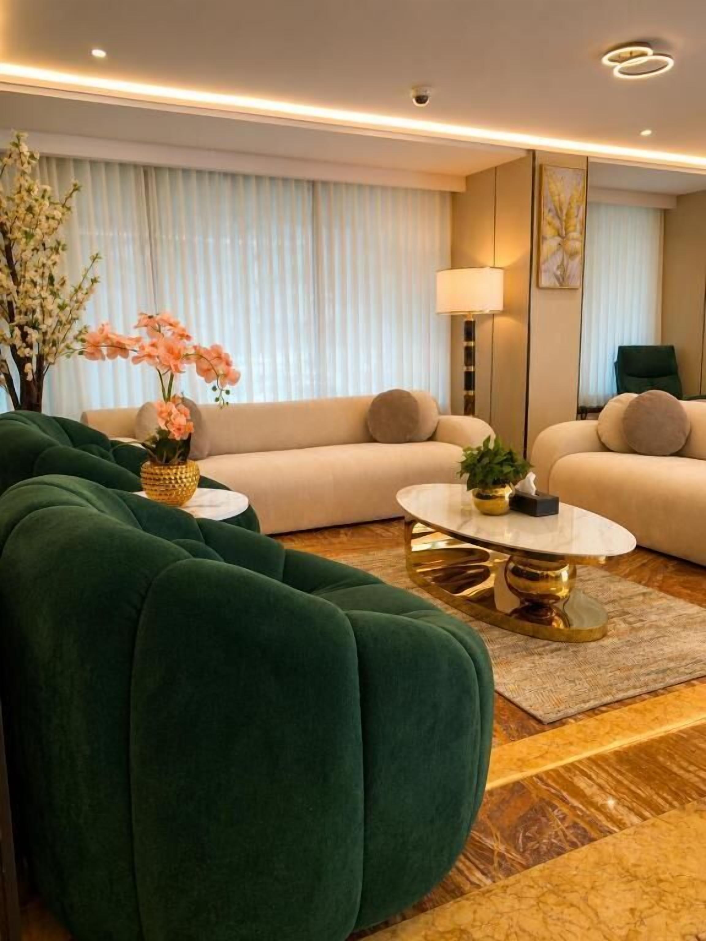 A modern living room with a green sofa, a beige sofa, and a round coffee table with gold accents.