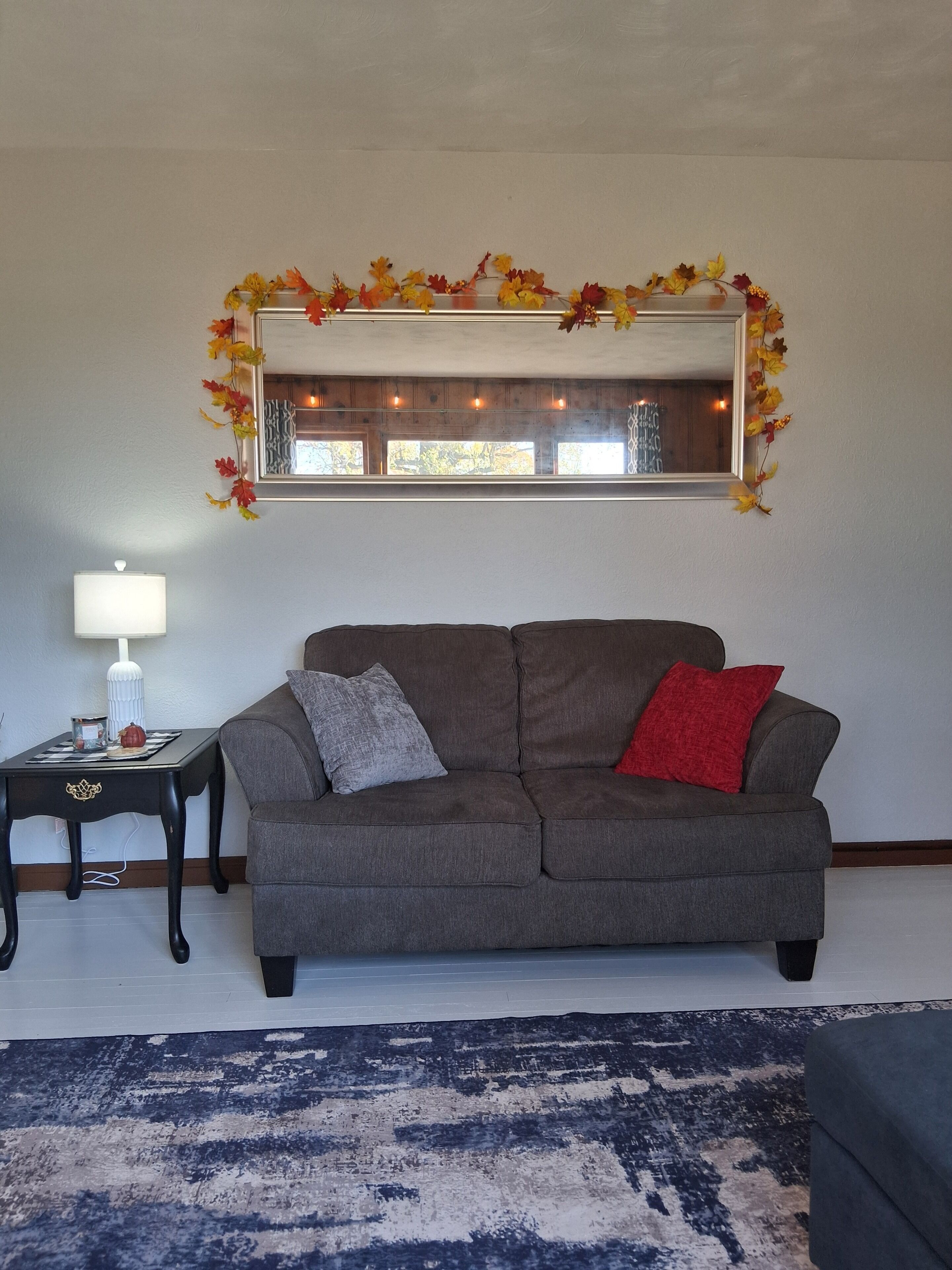 A living room with a gray sofa, a small side table, a lamp, and a patterned rug.