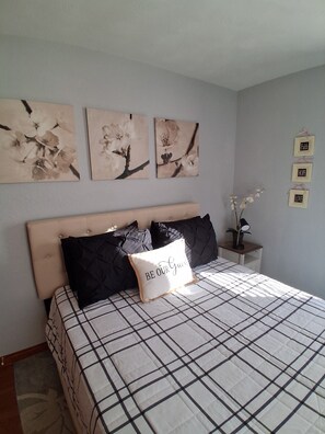Een slaapkamer met een bed, een hoofdbord en drie bloemende schilderijen aan de muur.