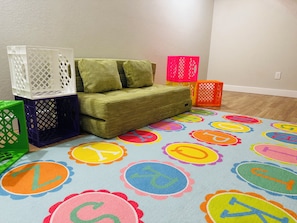 A room with a green sofa, colorful circular carpet, and storage bins.
