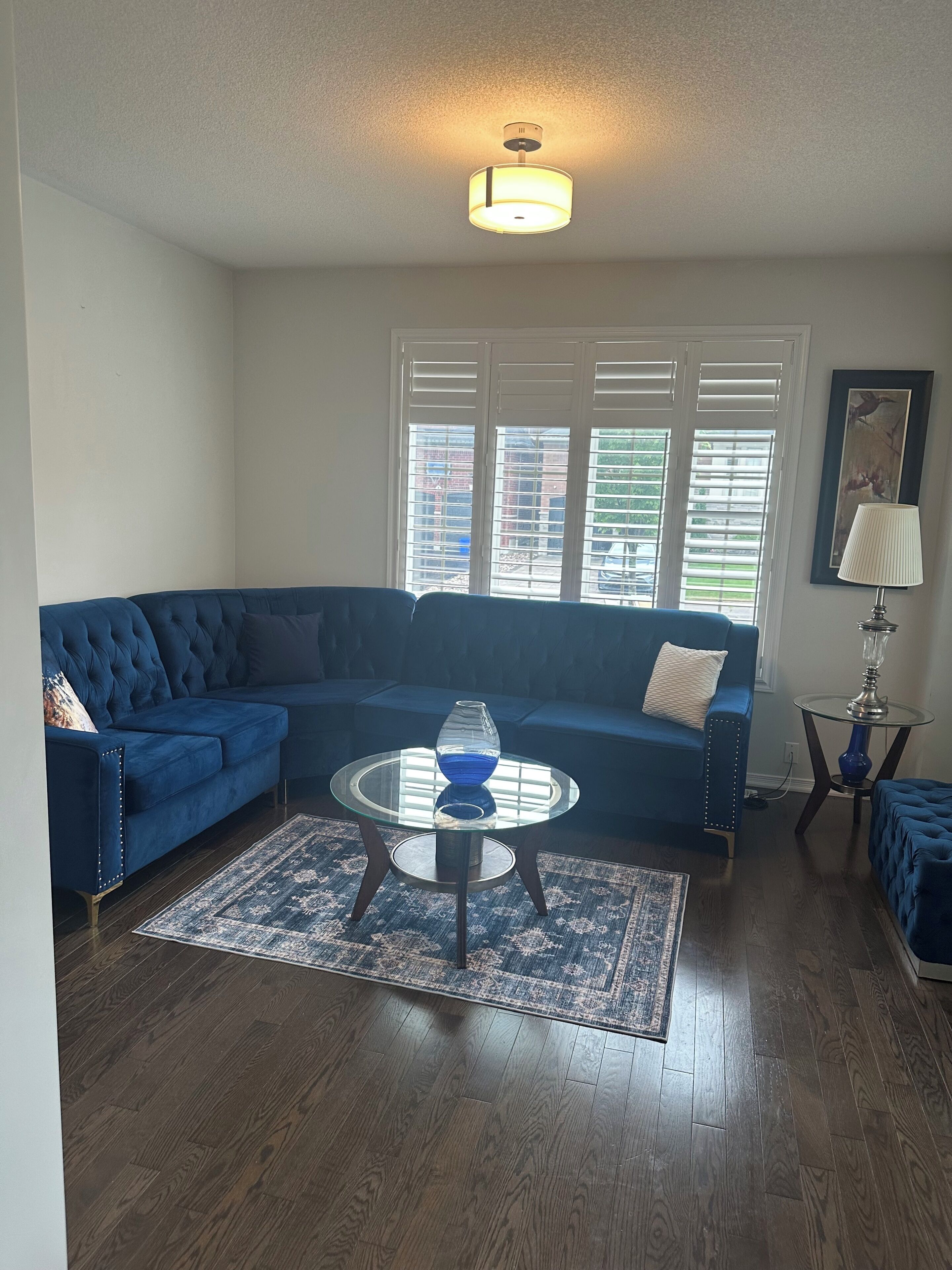 A living room with a blue sectional sofa, a glass coffee table with a blue vase, and a wooden floor.